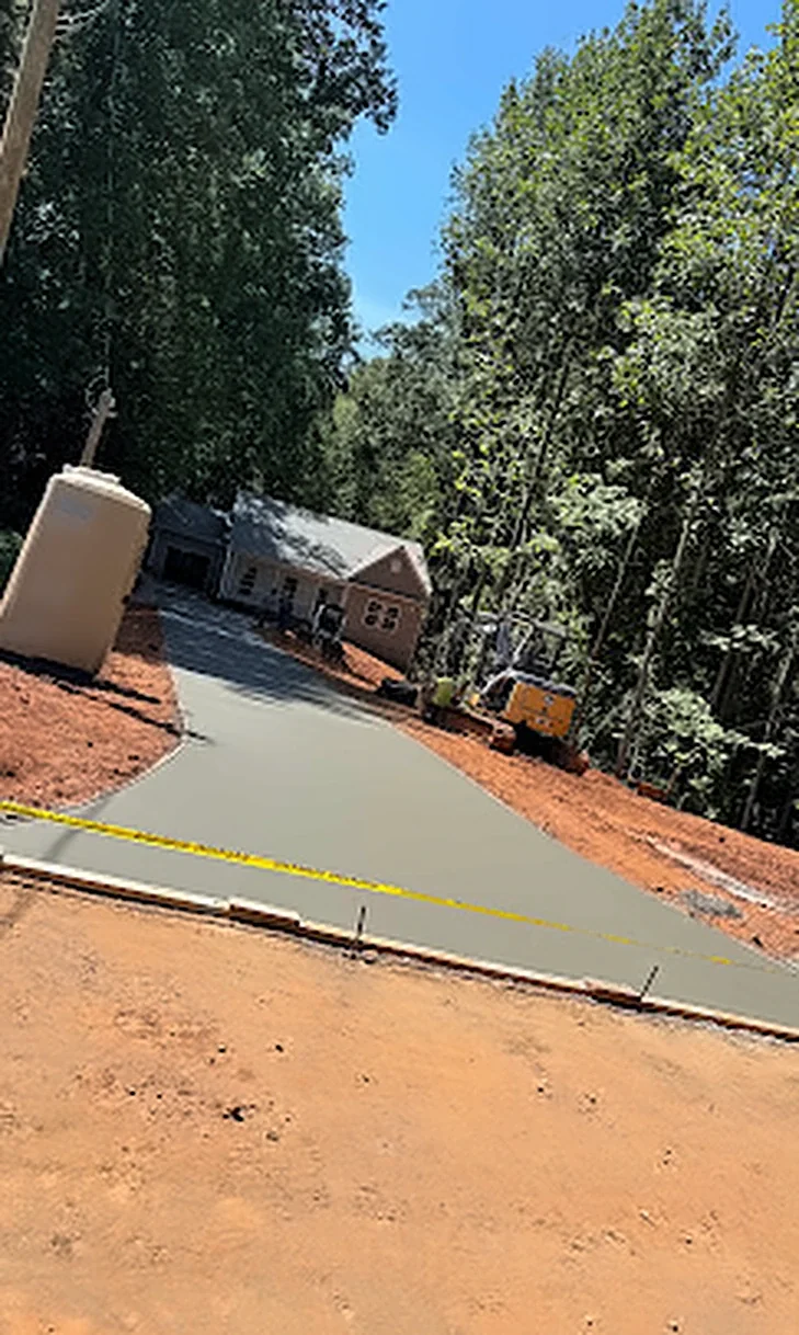 A long concrete driveway leading through the woods to a brick home