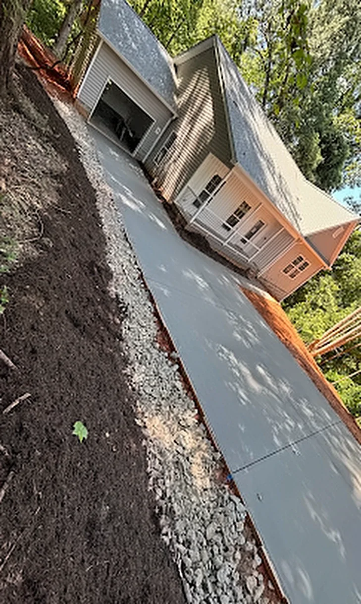 A new concrete driveway running down a slope to a newly built house