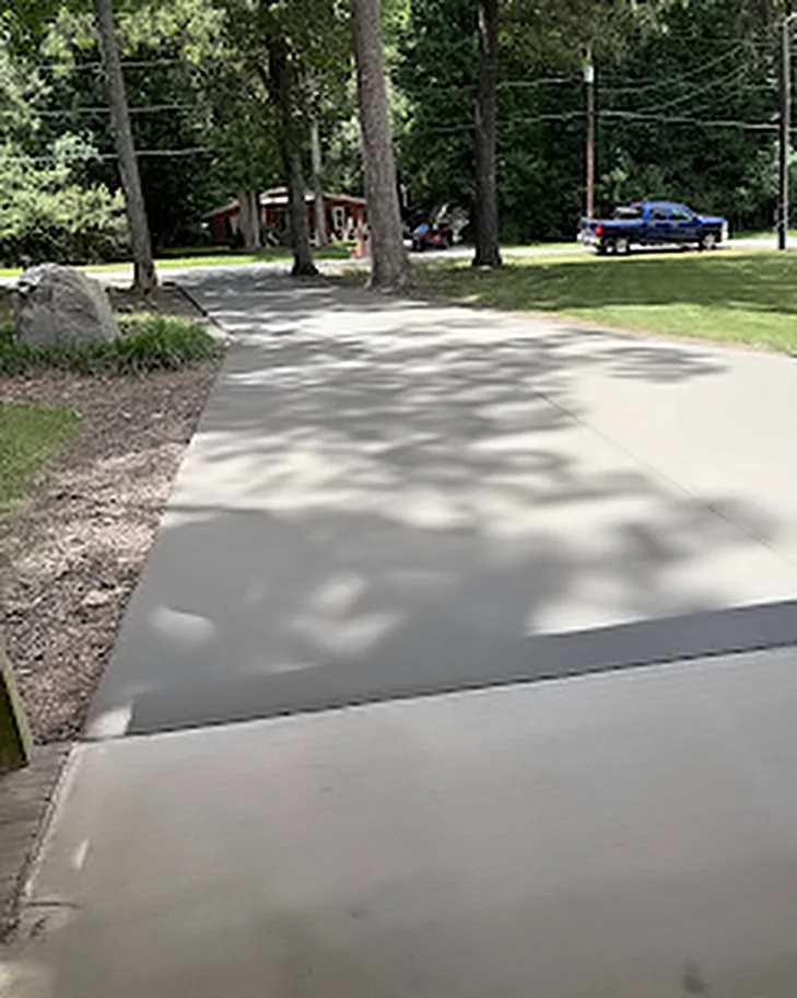 A wide concrete driveway and apron finished on a wooded lot