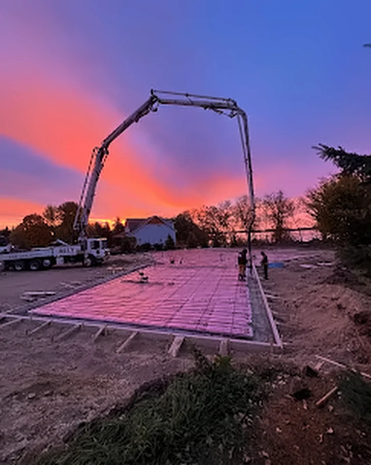 A concrete pump truck reaching over a formed foundation with rebar at sunset