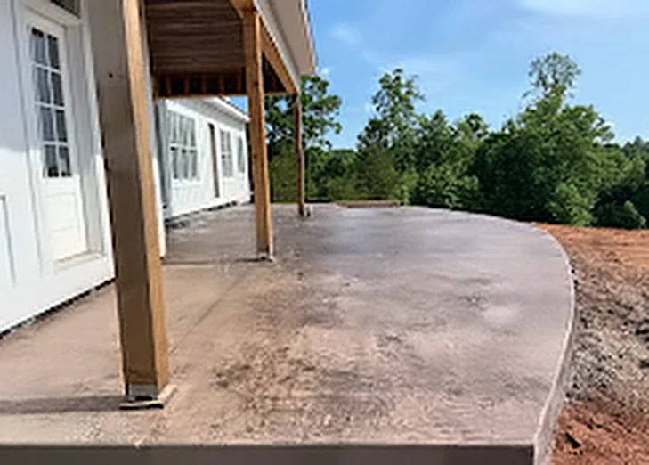A textured concrete patio with a rounded edge under a covered back porch