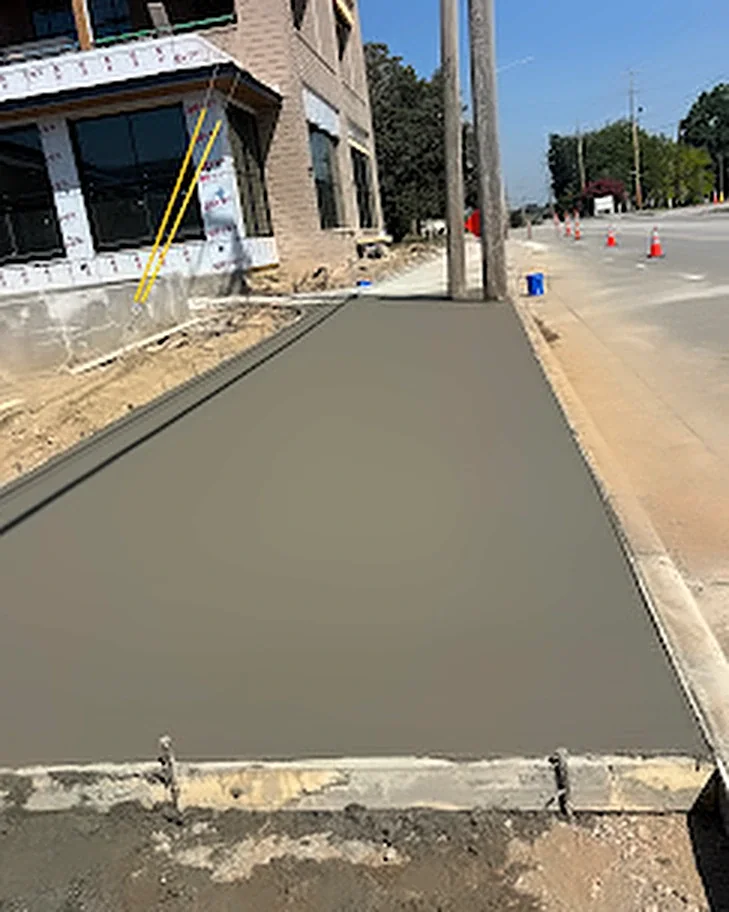 A new concrete sidewalk poured next to a brick commercial building