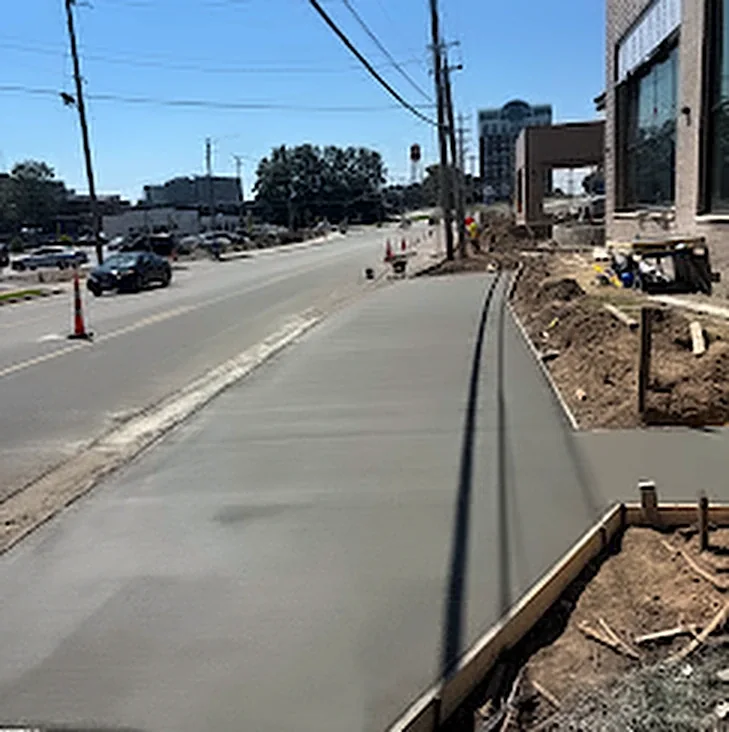 A long new concrete sidewalk running beside a city street