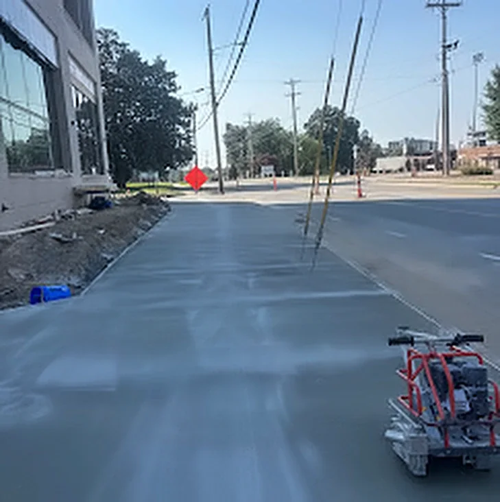 A wide concrete apron and sidewalk finished along a commercial street