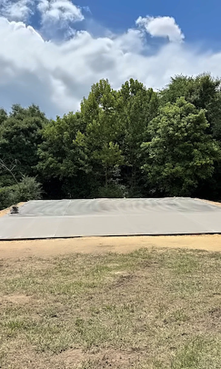 A finished concrete slab poured on an open lot lined with trees