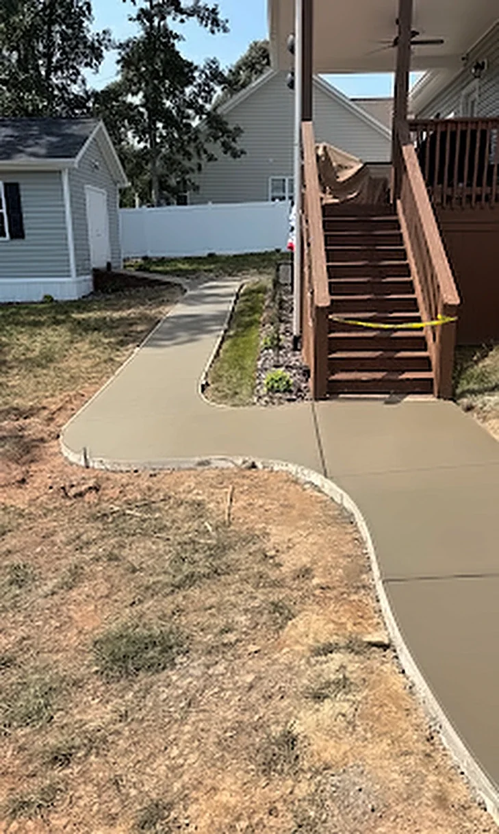 A concrete walkway wrapping around a house to a set of deck stairs